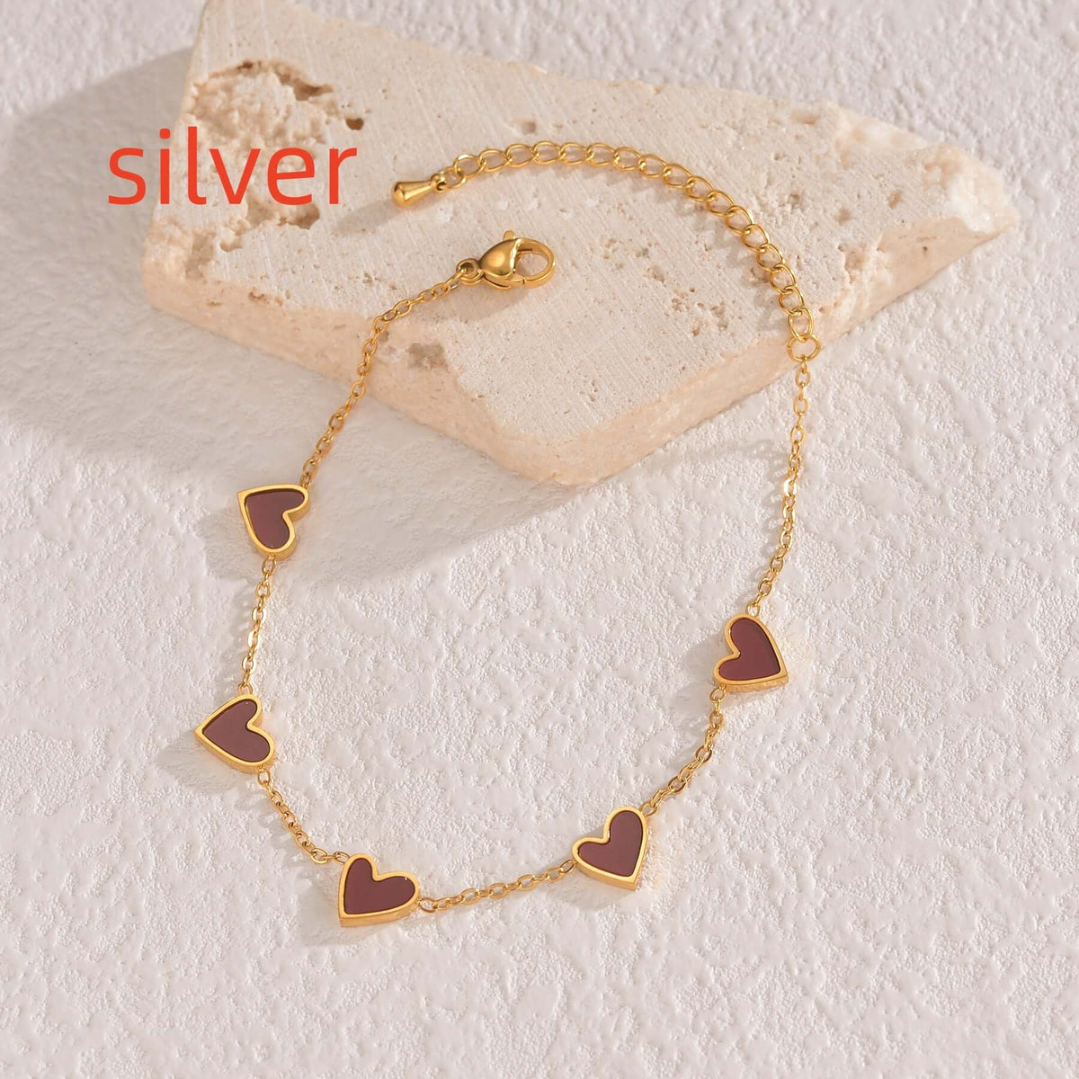 Gold bracelet with heart-shaped charms on a textured stone surface