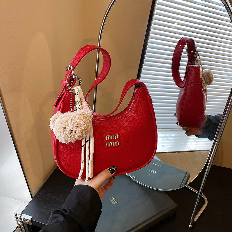 Woman wearing a vibrant red sparkly crescent hobo shoulder bag with a plush brown teddy bear charm hanging from the strap.