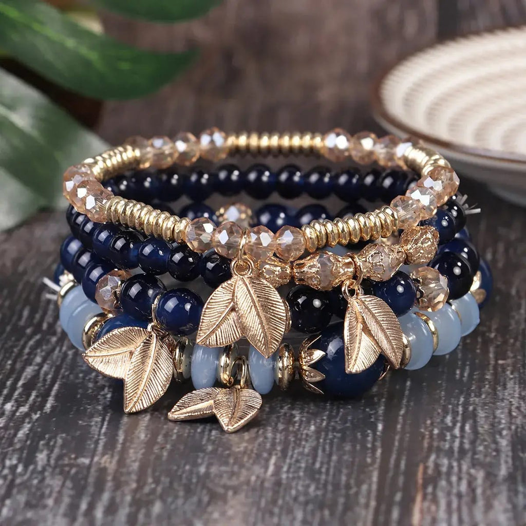 Stack of beaded bracelets with leaf charms on a wooden surface