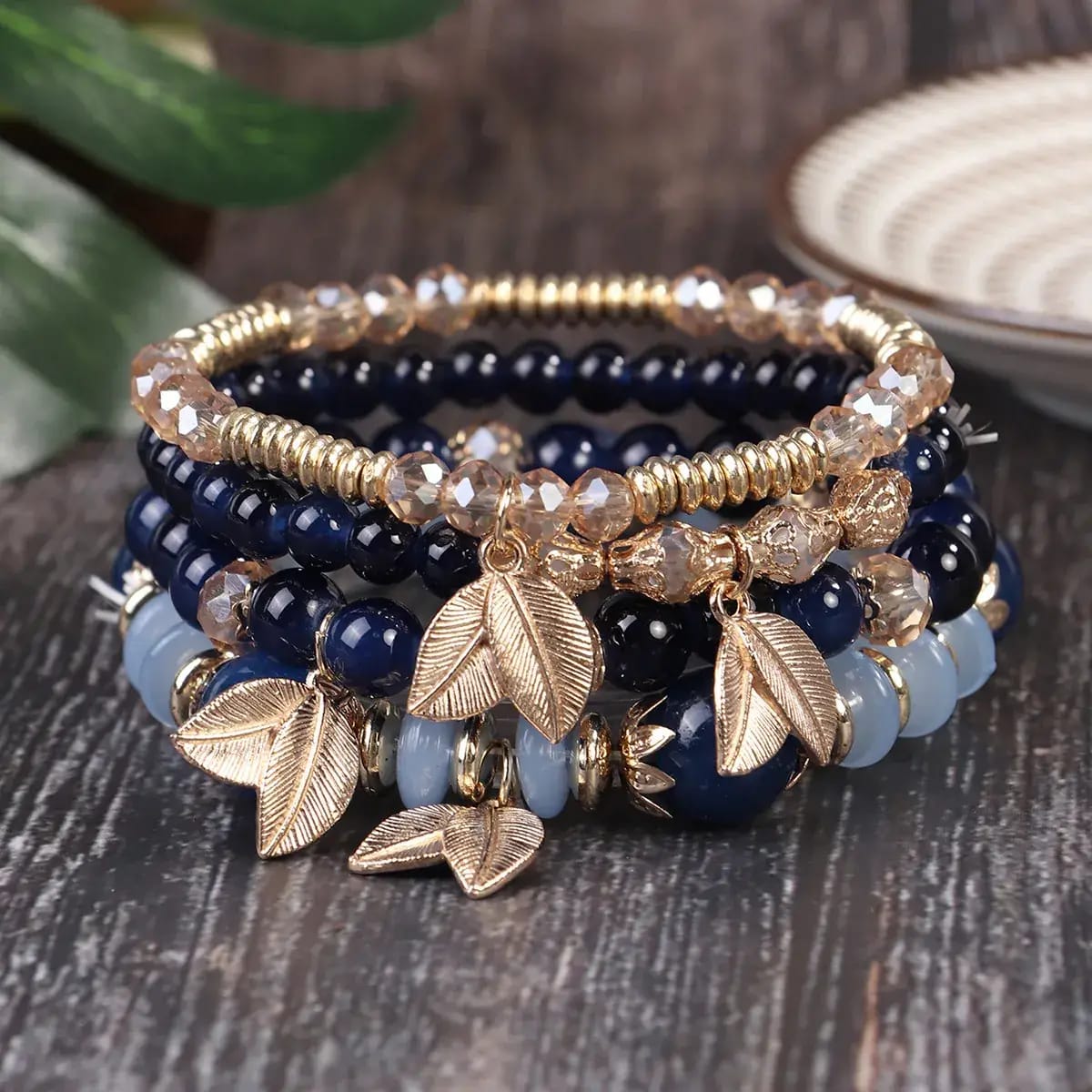 Stack of beaded bracelets with leaf charms on a wooden surface