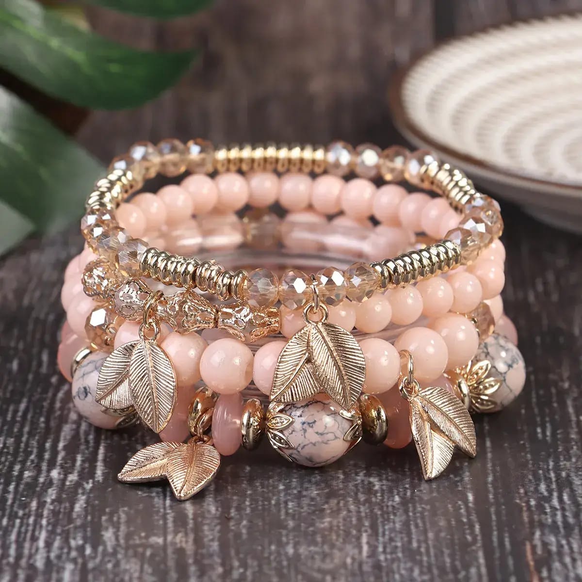 Stack of pink beaded bracelets with leaf charms on a wooden surface