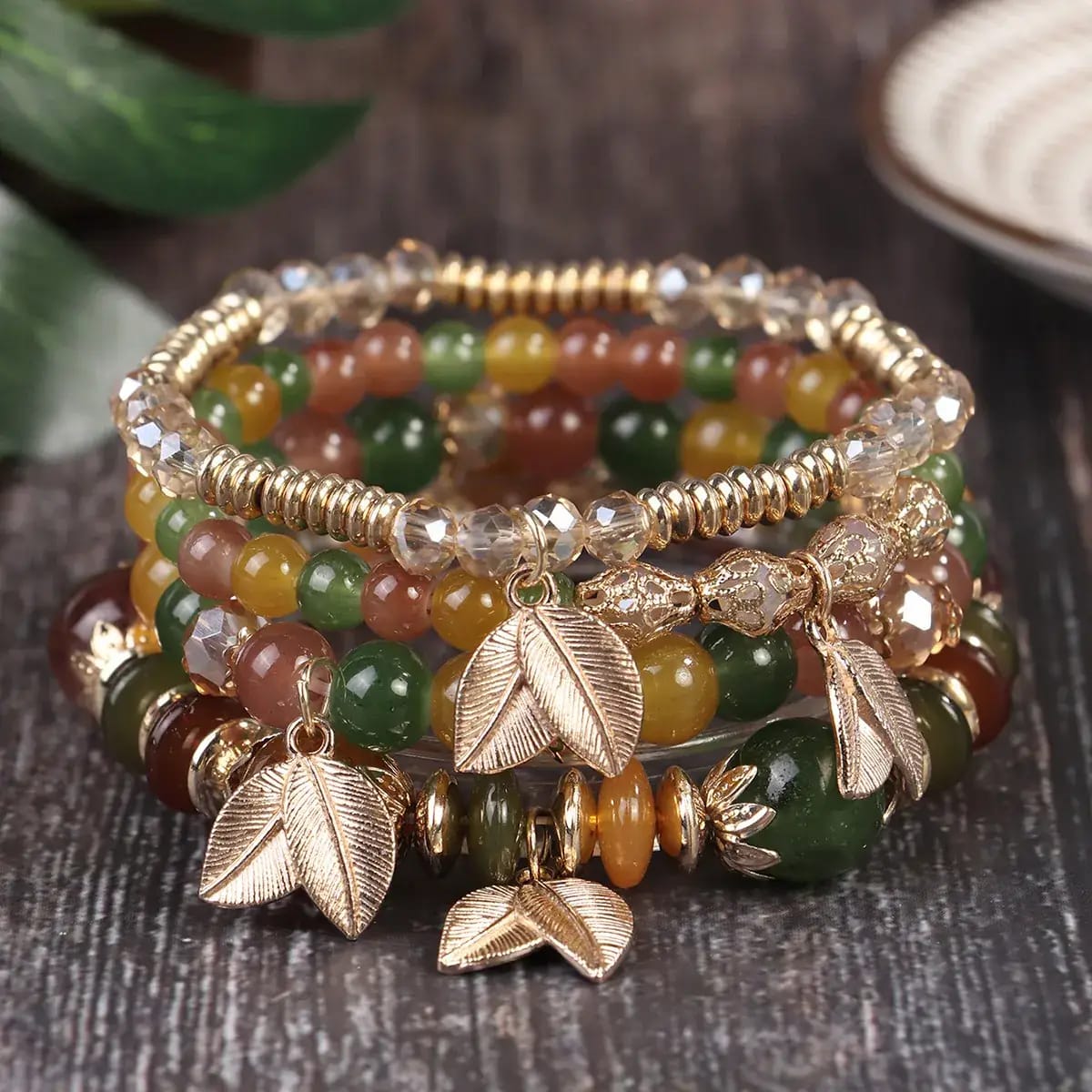 Stack of beaded bracelets with leaf charms on a wooden surface