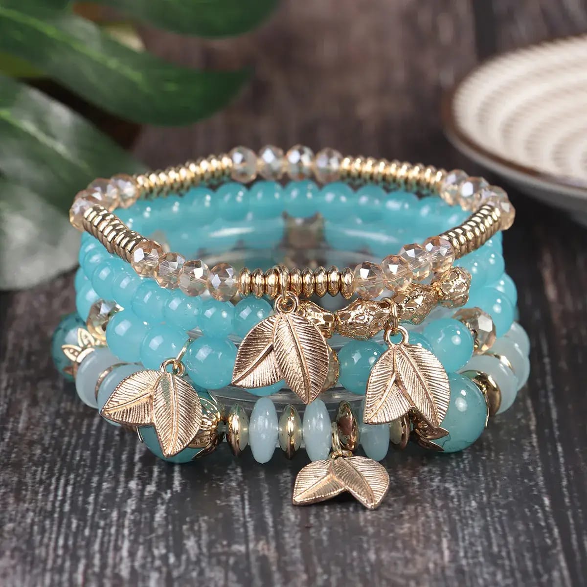 Turquoise beaded bracelet with gold leaf charms on a wooden surface