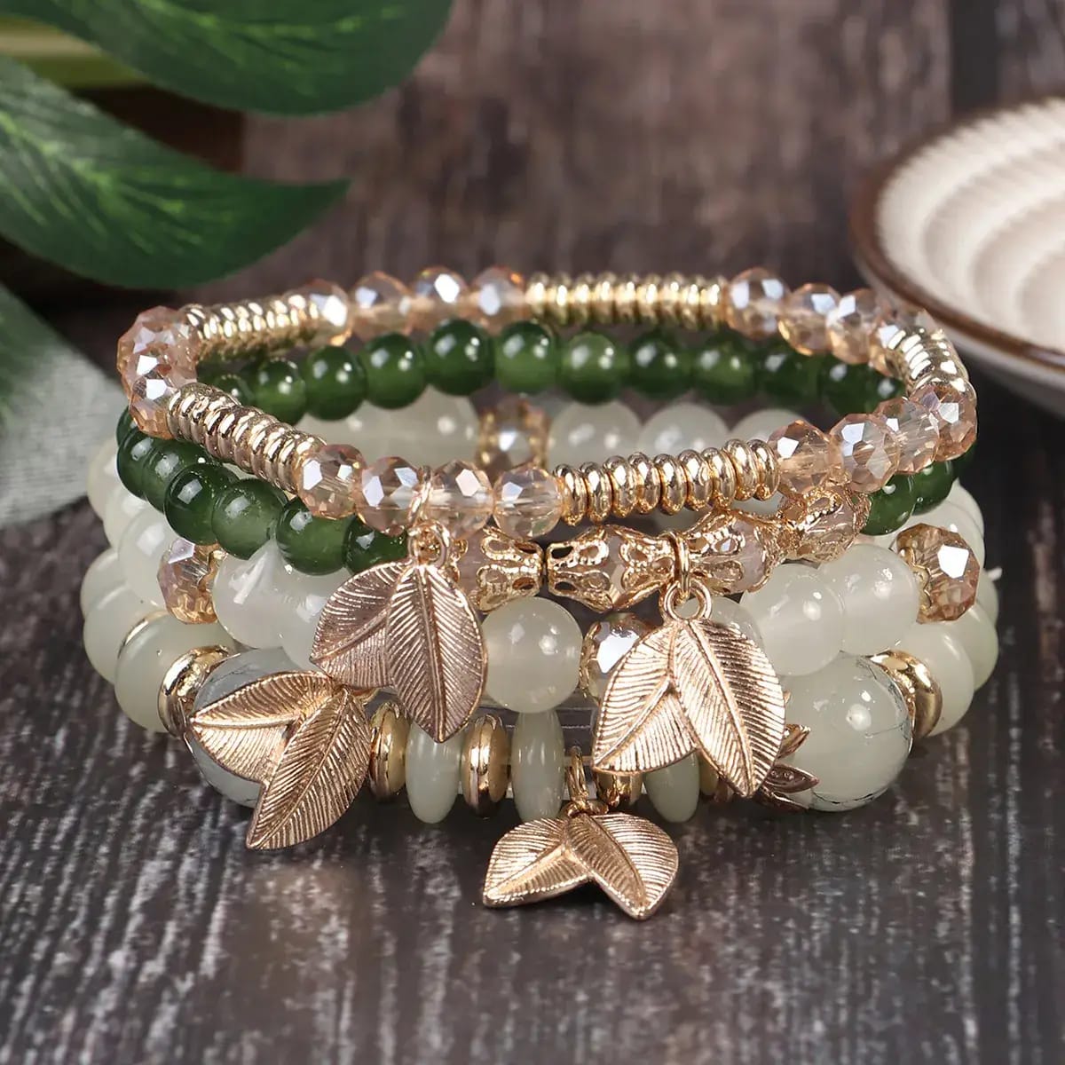 Stack of beaded bracelets with leaf charms on a wooden surface