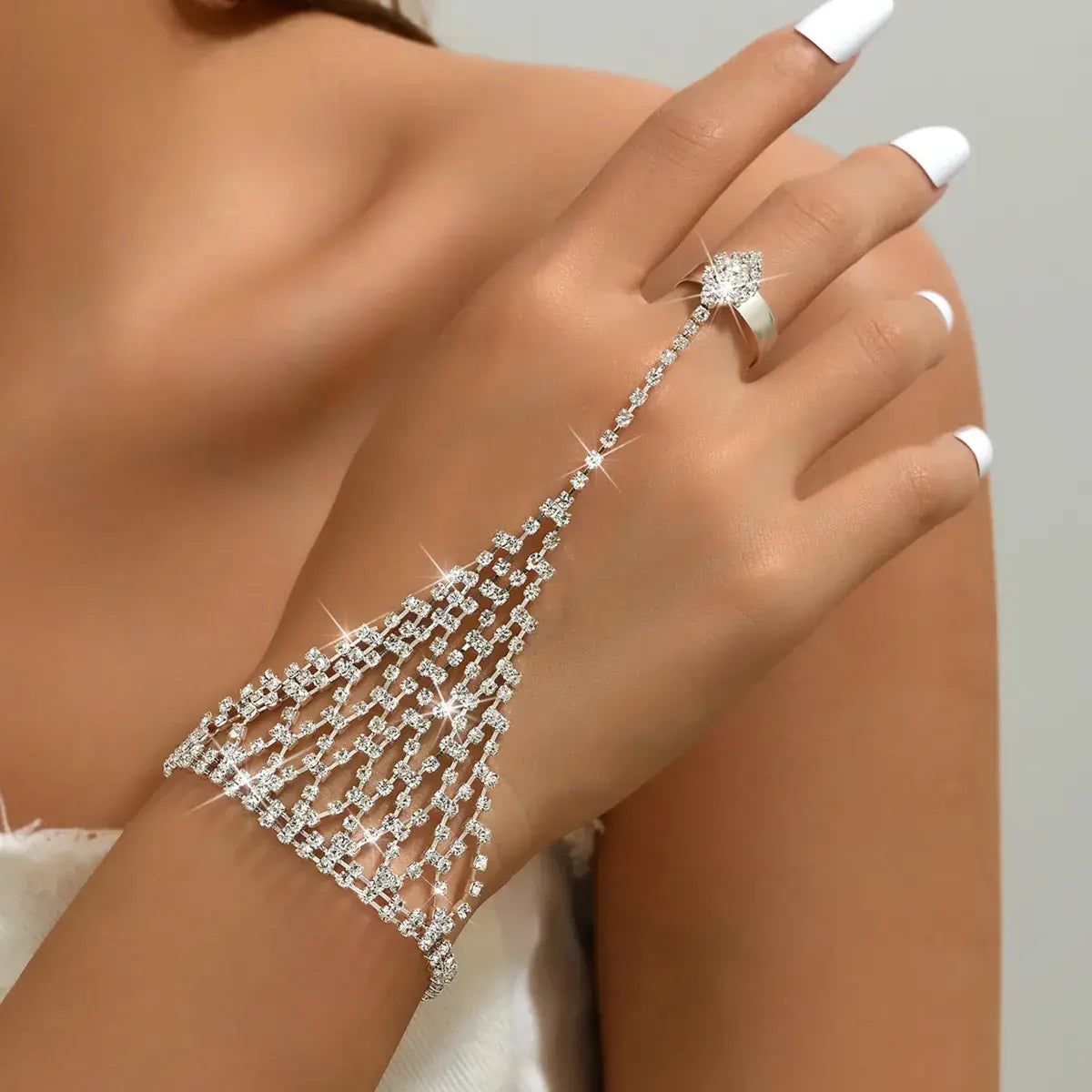 A close-up of a woman's hand and wrist wearing a sparkling silver rhinestone chain hand chain bracelet that drapes from the ring finger down to the wrist, paired with a matching silver ring.