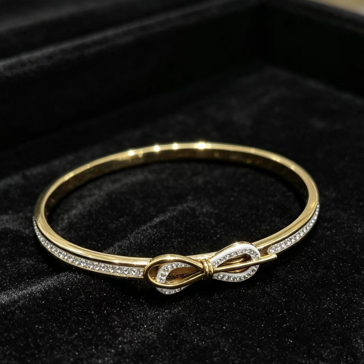 Gold infinity knot bangle bracelet displayed on black velvet surface