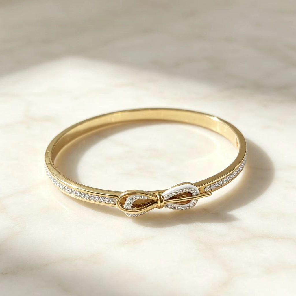 A gold bangle bracelet with a central infinity knot design, accented with pavé-set clear stones 