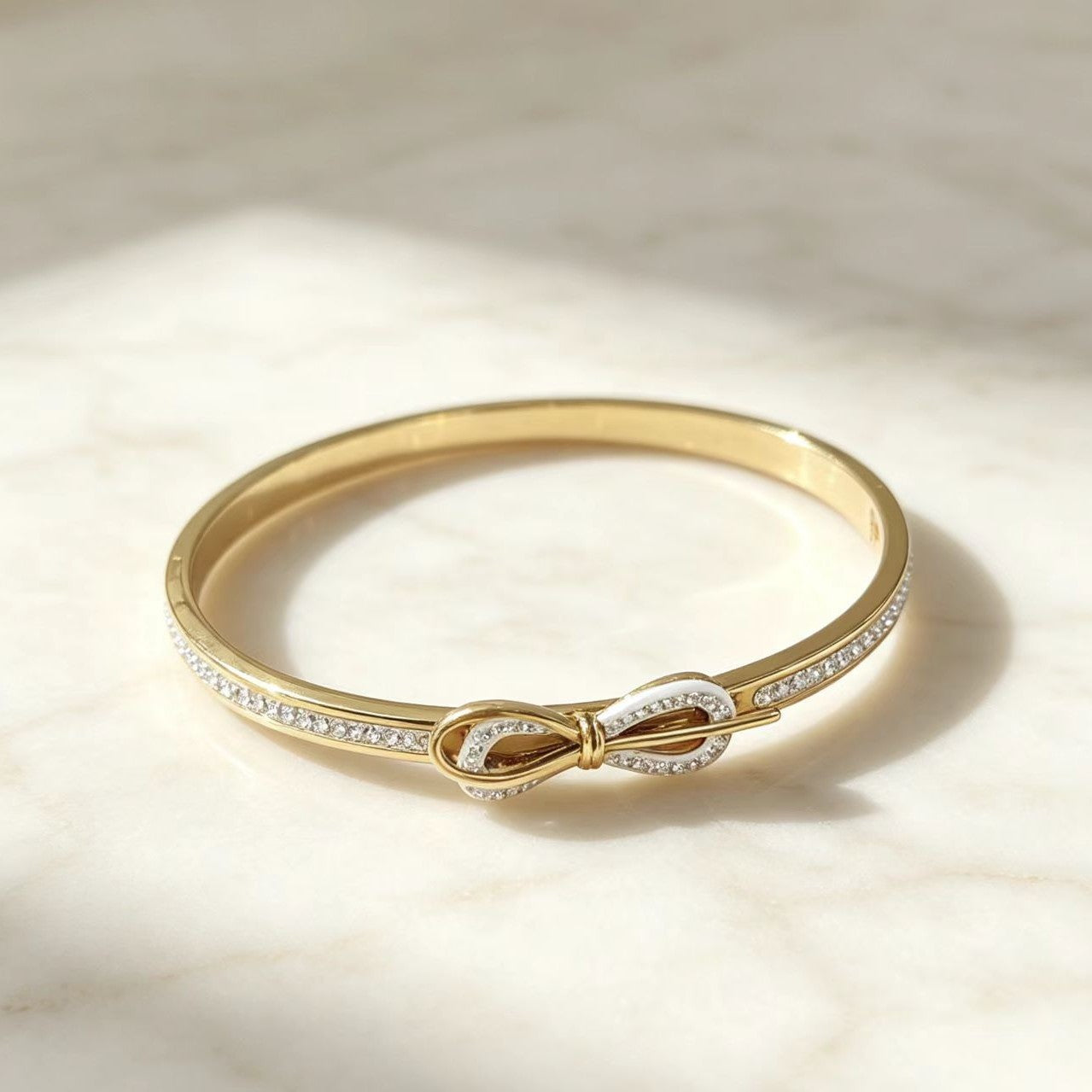 A gold bangle bracelet with a central infinity knot design, accented with pavé-set clear stones 