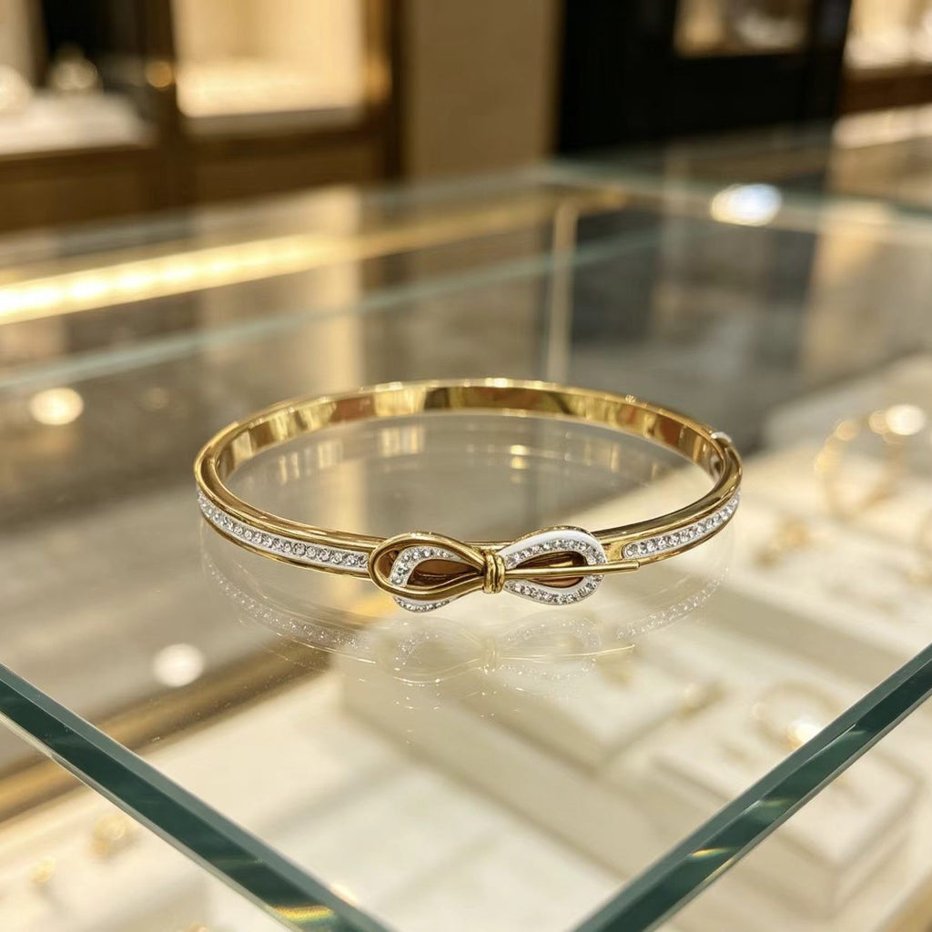 A gold infinity-style bangle bracelet with pavé-set clear stones, displayed on a glass jewelry case.