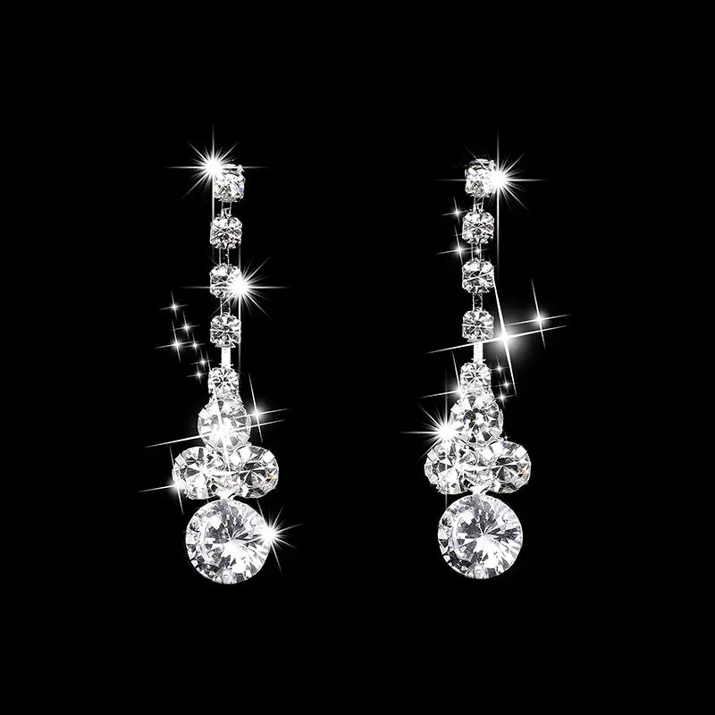 A pair of dangling diamond earrings with multiple round-cut clear stones arranged in a tiered, flame-like drop shape, shown on a solid black background with bright sparkle effects.