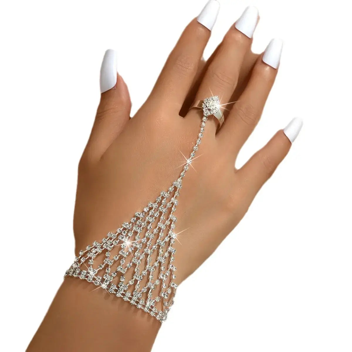 A silver-toned rhinestone chain hand chain worn on a hand with white manicured nails, featuring a matching ring, set against a plain white background.