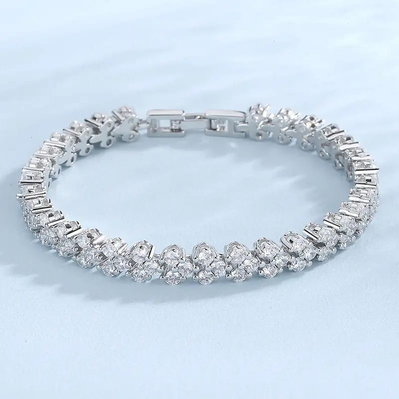 A silver-toned tennis bracelet with clear gemstones, arranged in a circular shape on a light blue background.