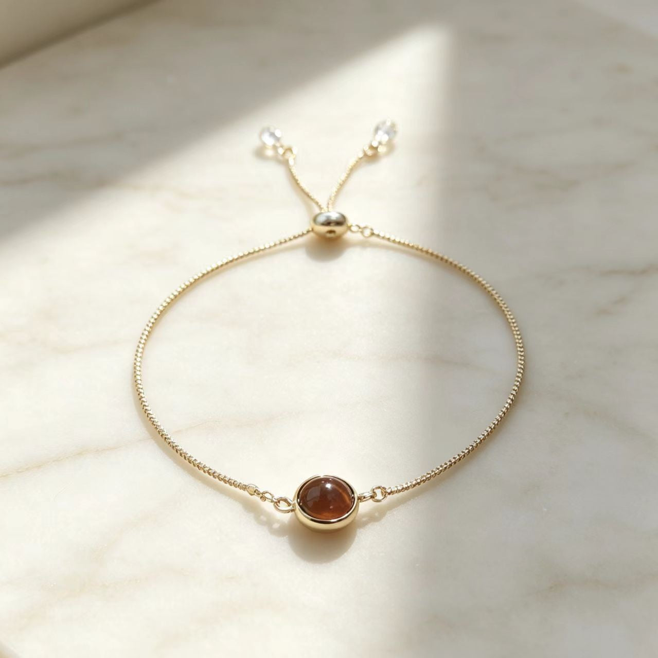 Adjustable gold bolo chain bracelet with round crystal charm under spotlight
