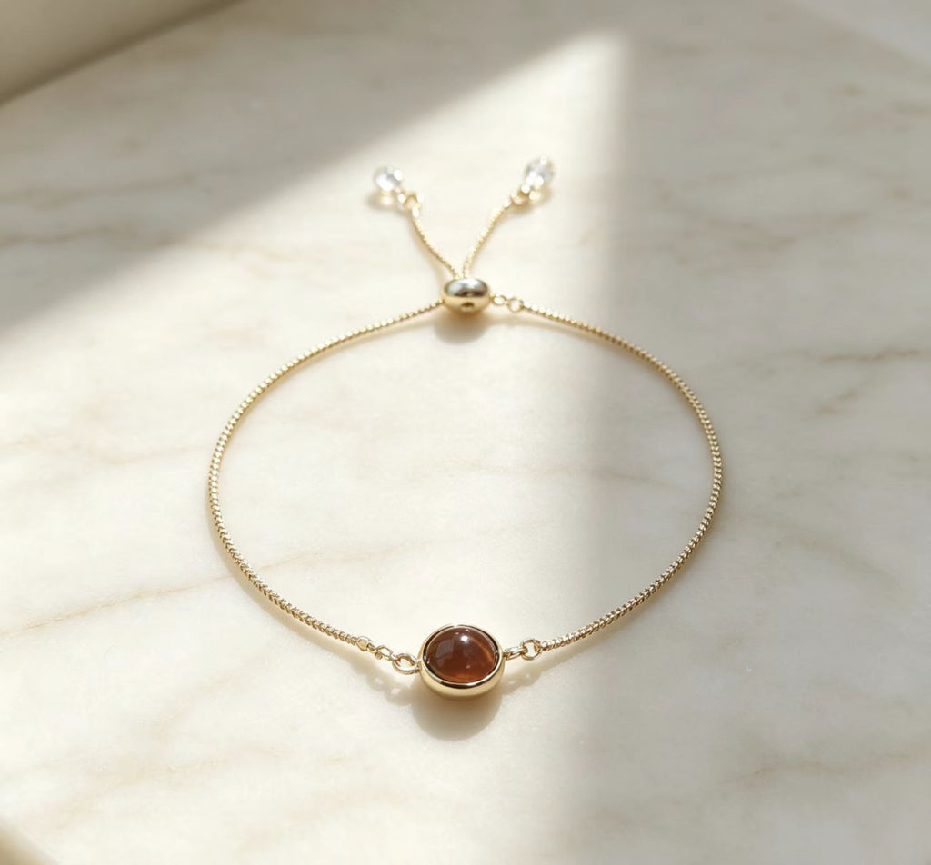 Adjustable gold chain bolo bracelet featuring round red crystal charm