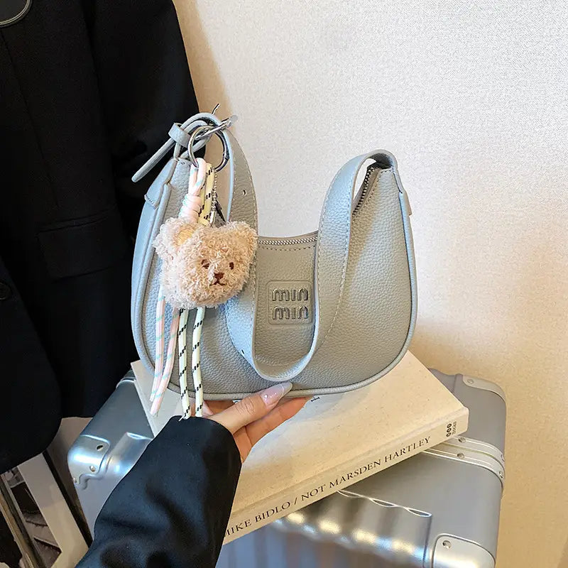 Hand holding a shimmering light blue silver hobo purse with a plush teddy bear key ring accessory.