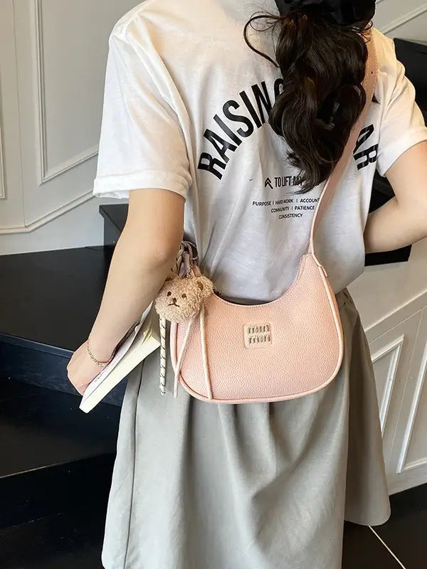Model wearing a light pastel pink sparkly crescent shoulder bag featuring a cute stuffed bear bag charm.