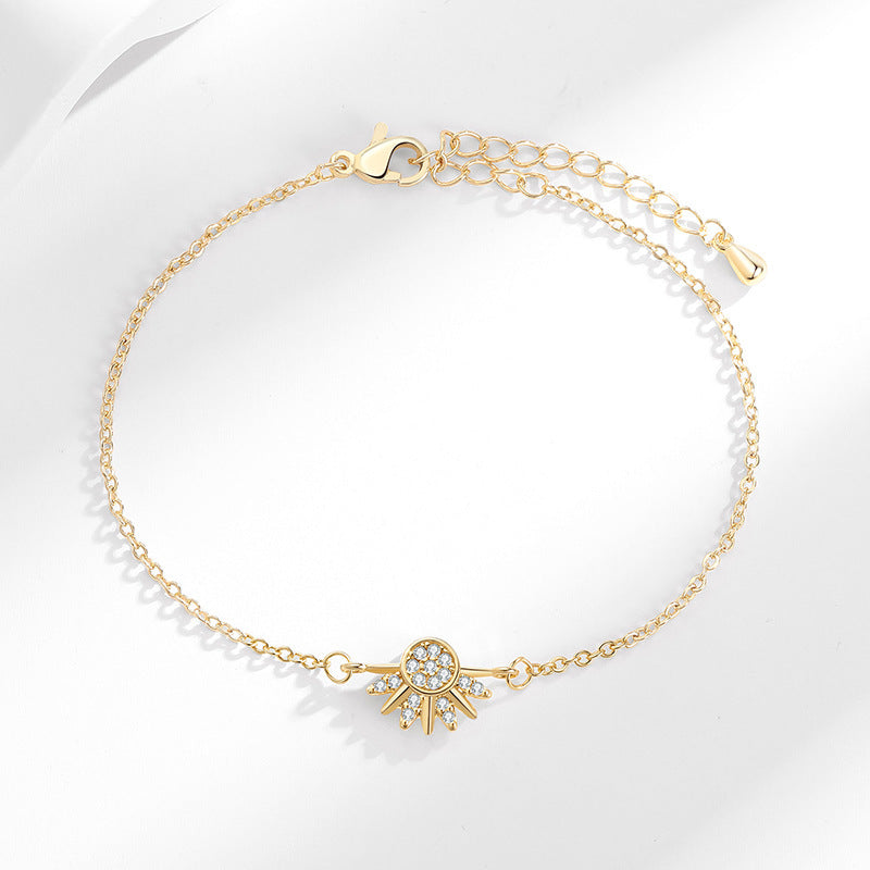 Close-up of delicate gold chain bracelet with sun charm and blue crystal evil eye detail
