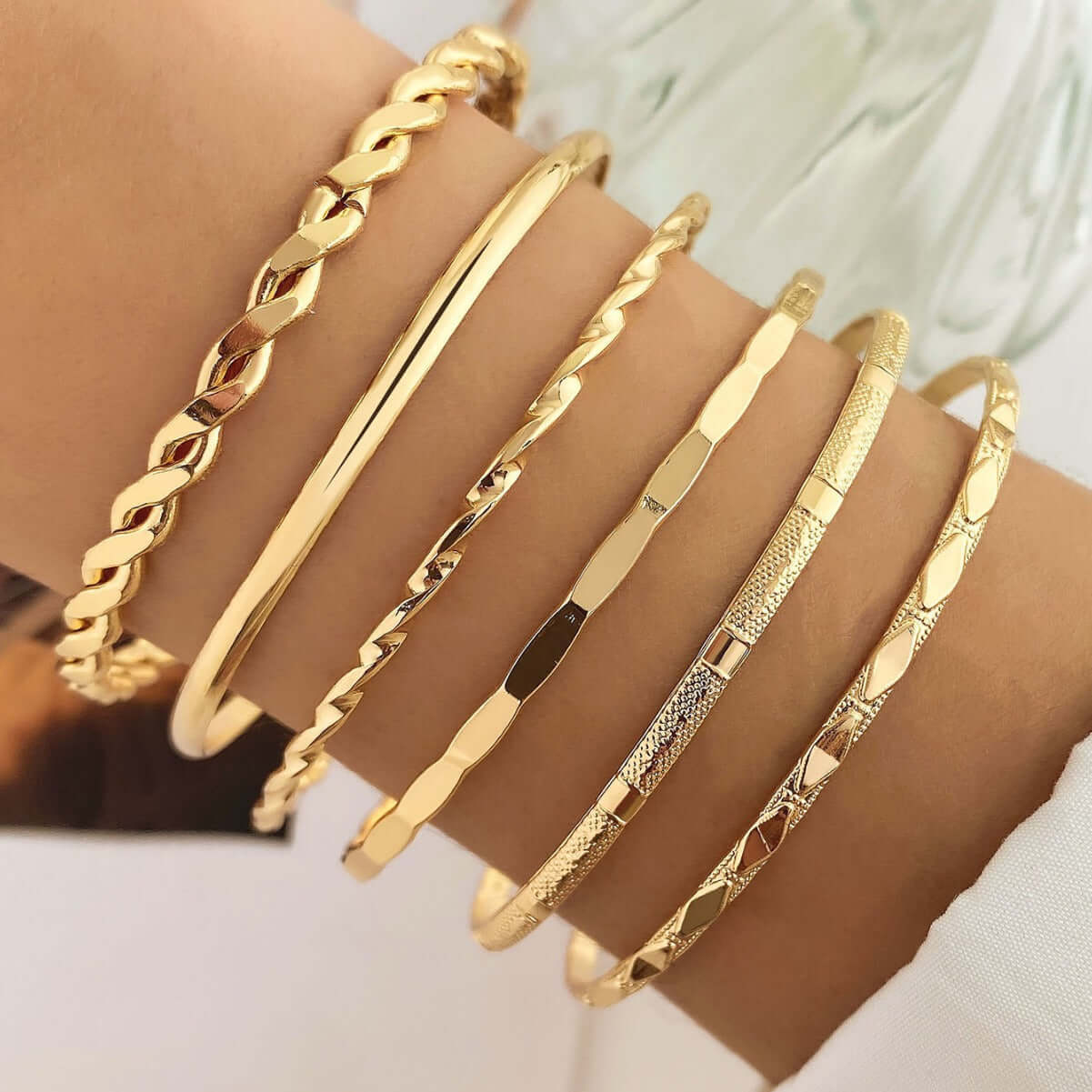 Gold bracelets on a wrist with a neutral background