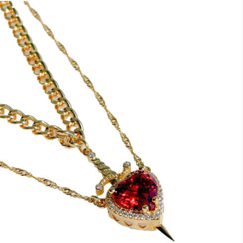 Gold necklace with a red heart-shaped gemstone pendant on a white background