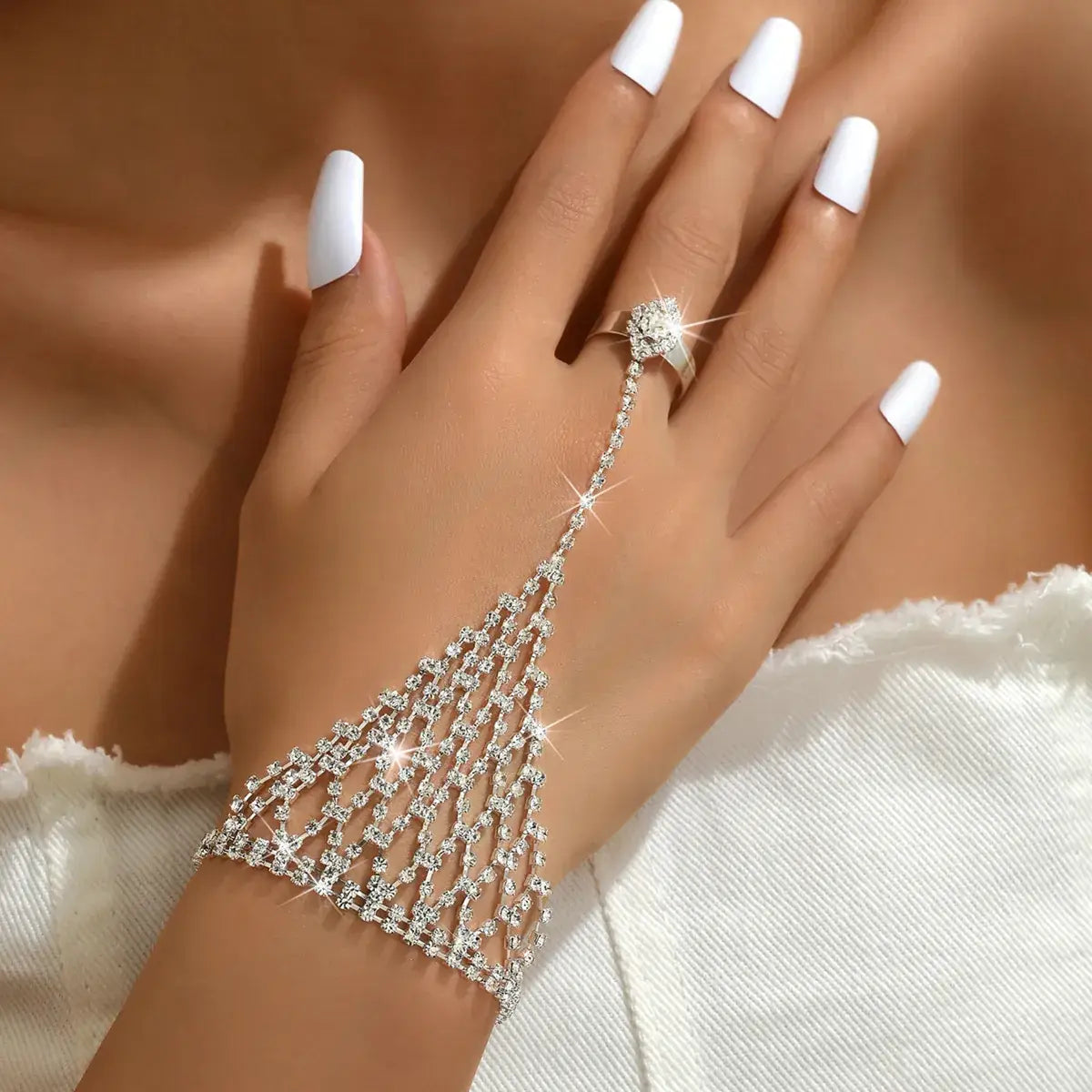 Hand wearing a sparkling silver bracelet and ring with white nail polish on a neutral background