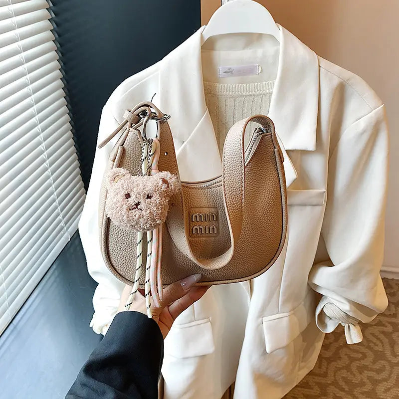 Hand holding a neutral khaki beige glitter crescent shoulder purse set against a light background.