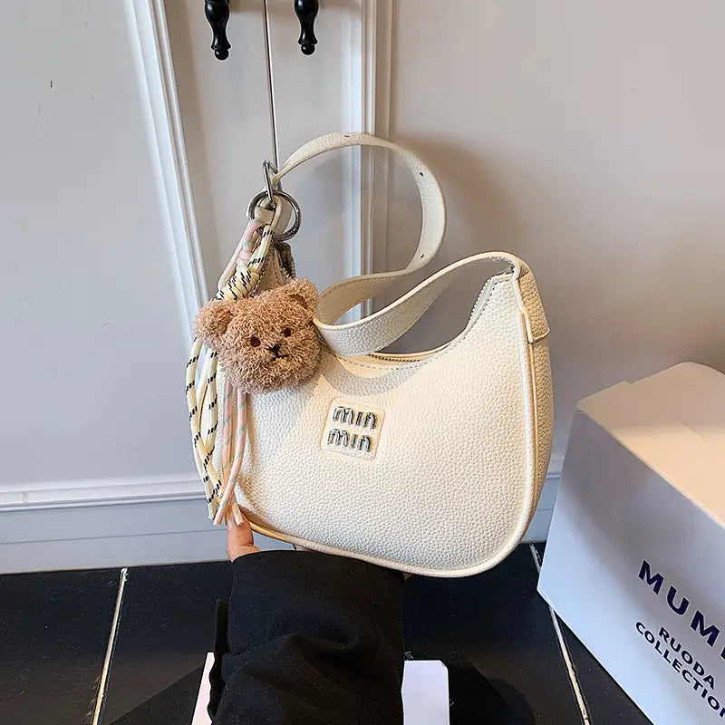 Hand holding a neutral khaki beige glitter crescent shoulder purse set against a light background.