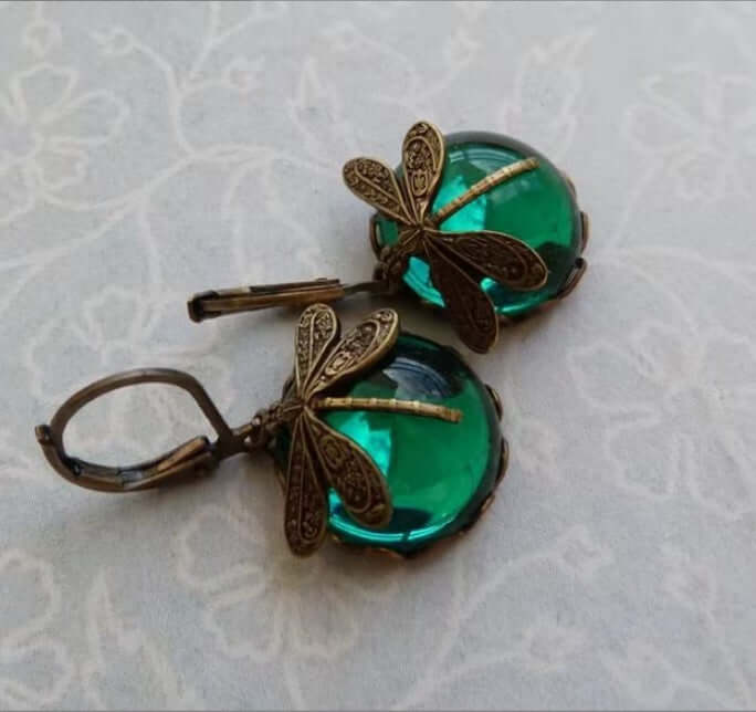 Pair of dragonfly-themed earrings with green gemstones on a textured white background