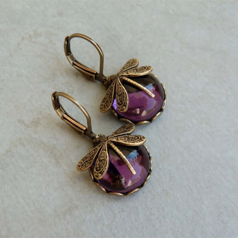 Pair of gold earrings with purple gemstones on a textured light background