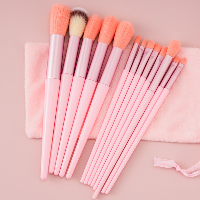 Pink makeup brushes arranged diagonally across a two-tone pink surface.