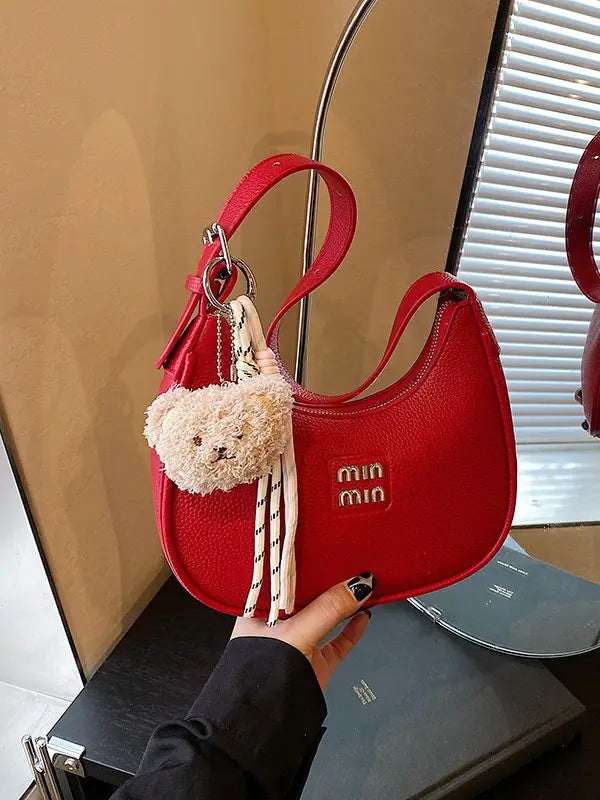 Close-up of a hand holding a red glitter hobo bag with gold hardware, textured fabric, and a plush bear accessory.