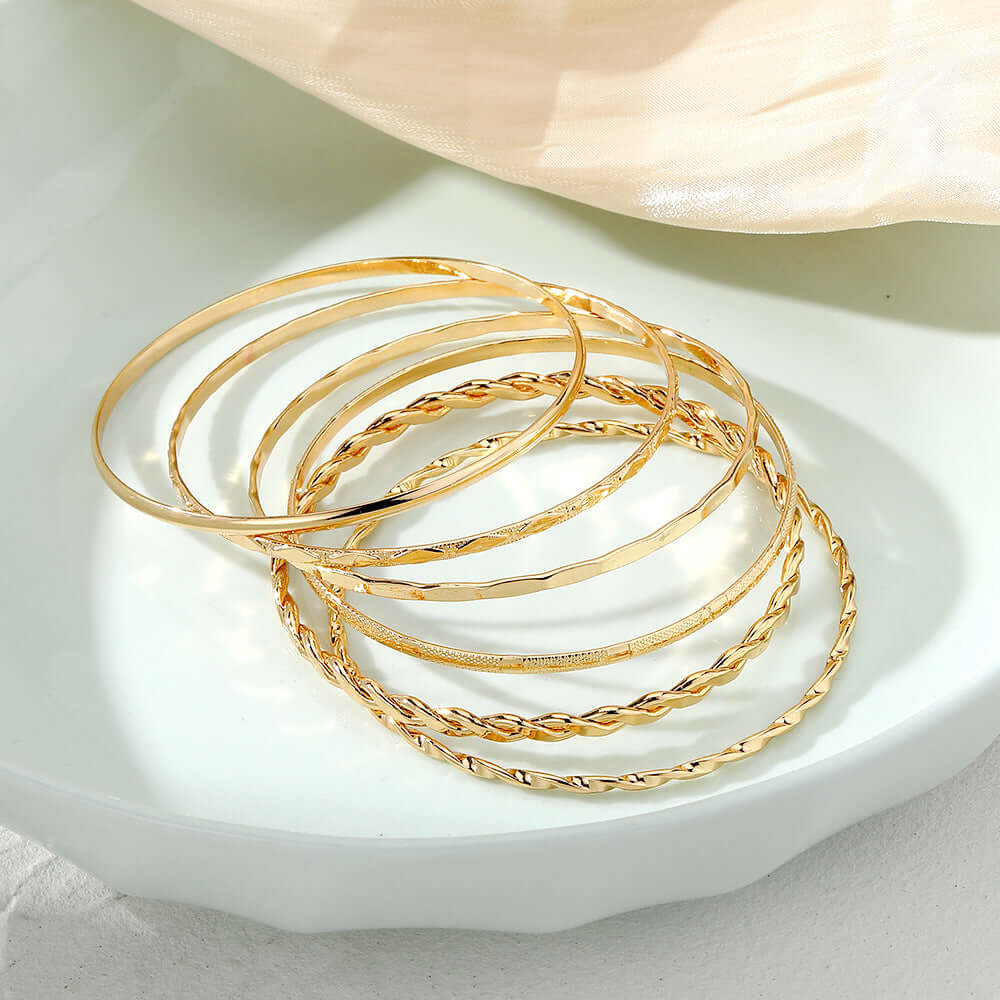 Set of gold bangles on a white dish with a beige fabric background