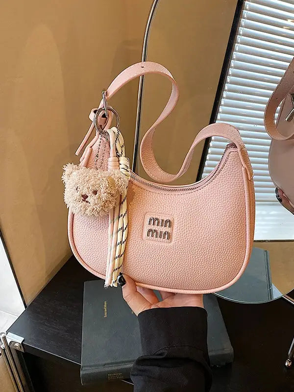 Hand holding a baby pink glitter hobo bag with a shoulder strap and attached teddy bear keychain.