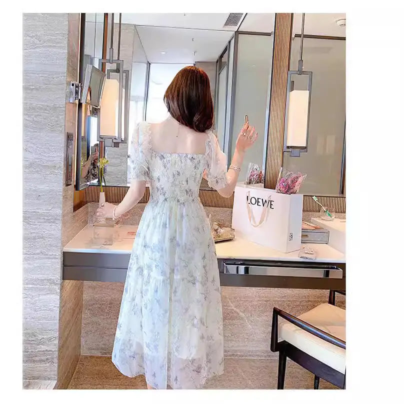Woman in a floral dress standing in front of a mirror with a Loewe bag on a counter.