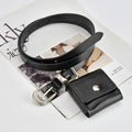 A black leather belt with a silver buckle, shown coiled on top of a magazine page next to a matching black leather card holder pouch.