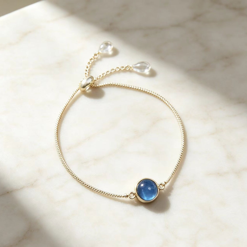 Delicate gold chain adjustable bolo bracelet with round blue crystal charm on light background