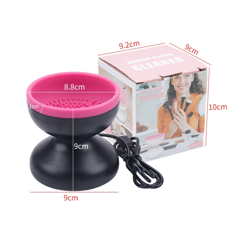 Black and pink electric makeup brush cleaner unit standing next to its retail packaging box and USB cable.