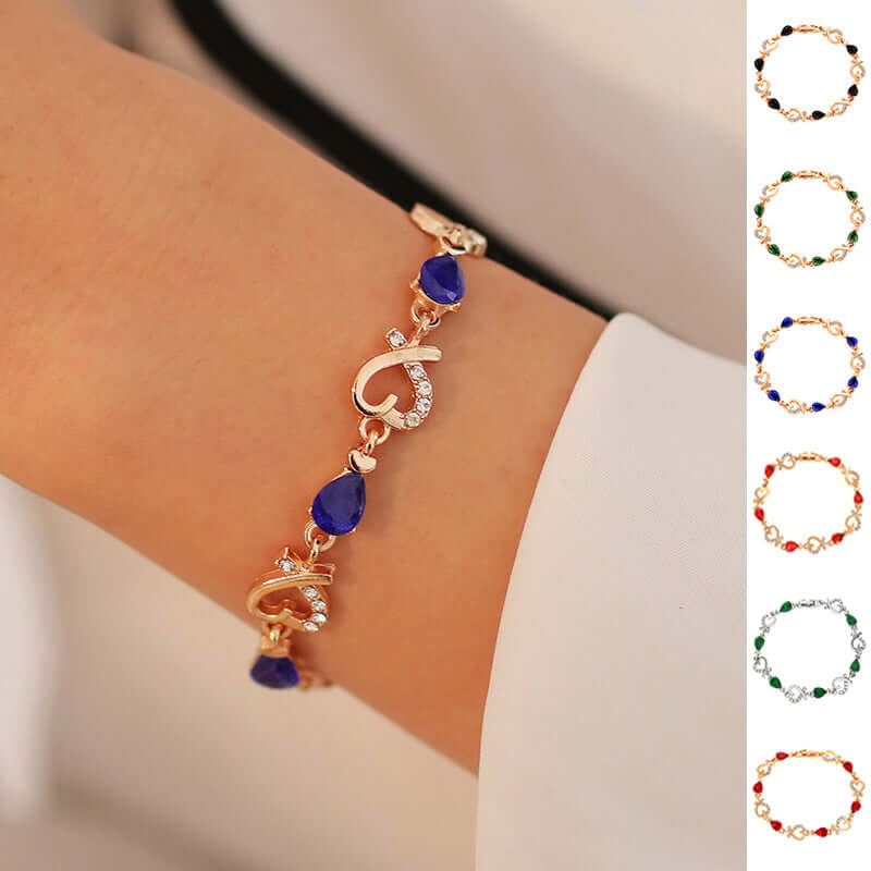 Close up of a woman wearing a gold link bracelet featuring deep blue teardrop crystals.