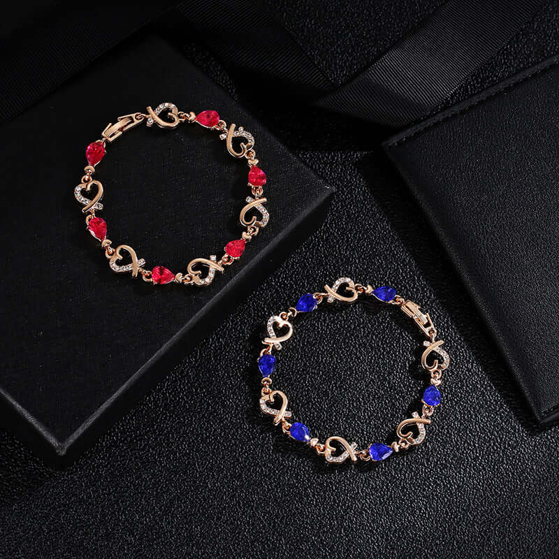  Pair of gold link bracelets with red and blue teardrop crystal accents on a black background.