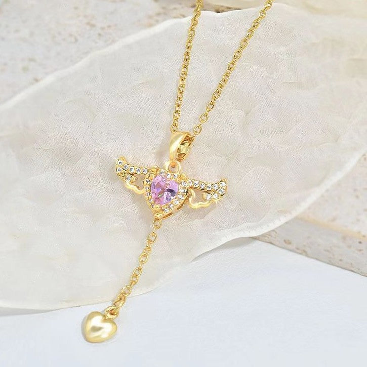  Gold y-lariat necklace with pink heart crystal and spread angel wings on a light blue background.