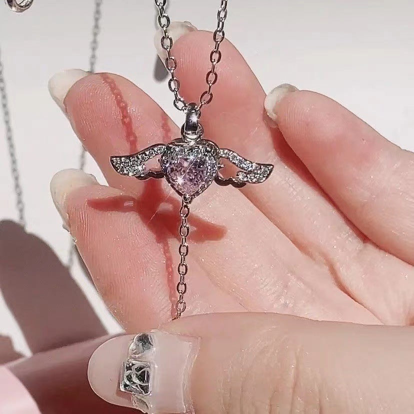 Hand holding a silver pink heart necklace showing the drop tassel chain and wing detail.