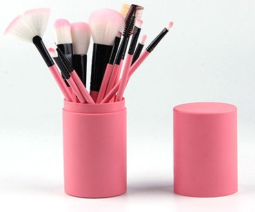 Set of makeup brushes in a pink holder on a white background