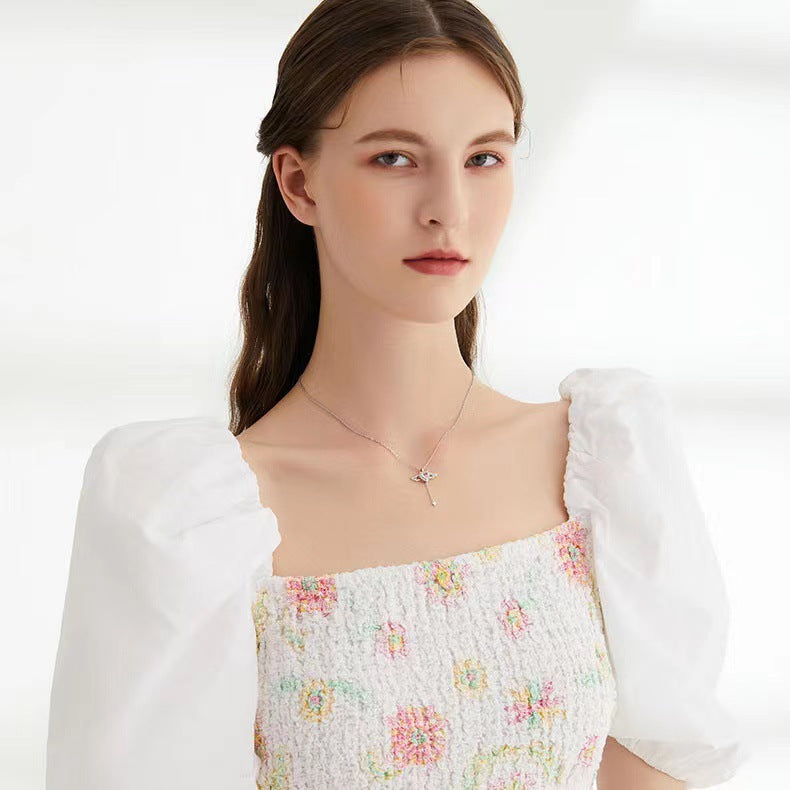 Model wearing a silver movable angel wing necklace with a pink heart gemstone pendant.