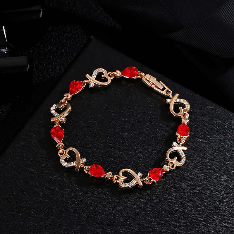  Gold link charm bracelet with vibrant red teardrop crystals on a dark surface.
