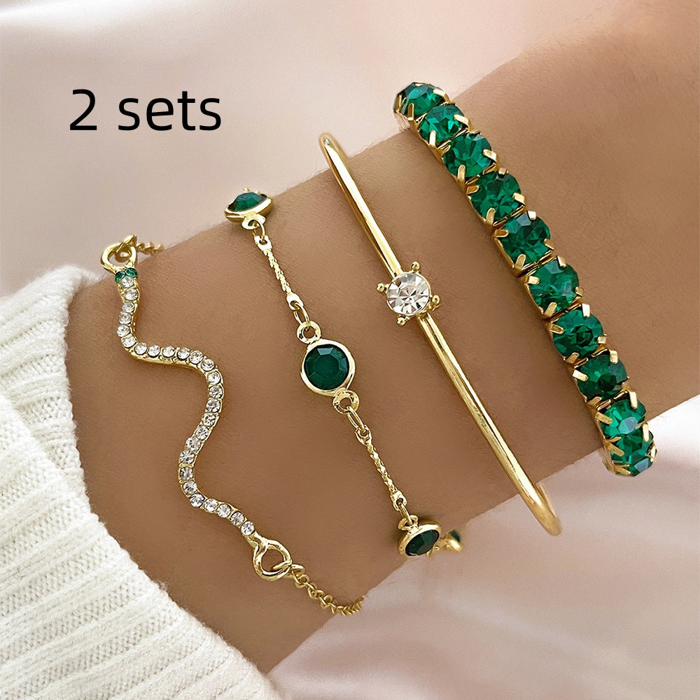 Two sets of gold and emerald green layered bracelets arranged together on a beige fabric background.