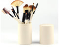 White cylindrical makeup brush holder standing open with brushes neatly stored inside